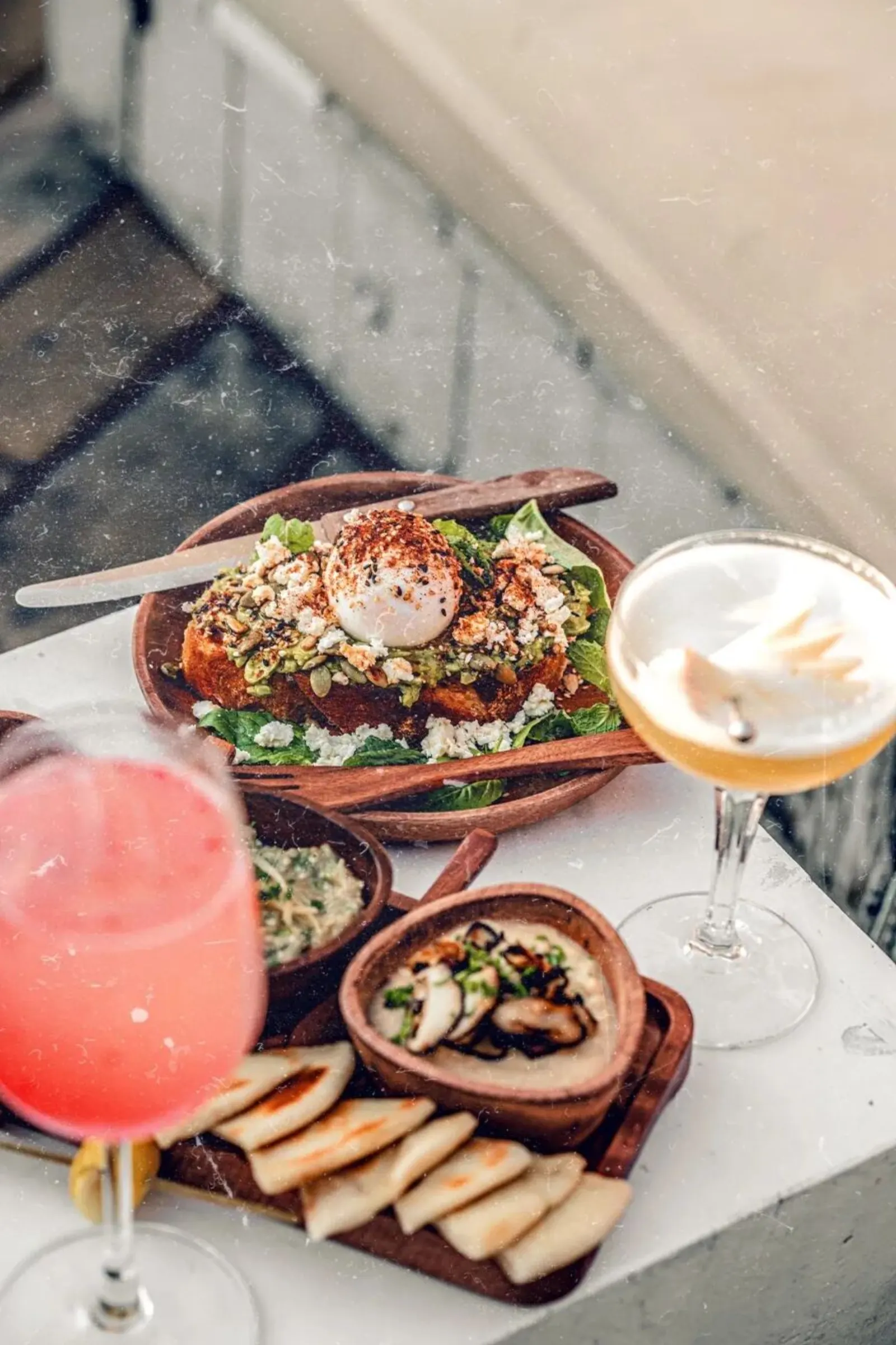 Cocktail và đồ ăn tại Banana Mama: avocado toast, mezze platter và hai ly cocktail tươi sáng