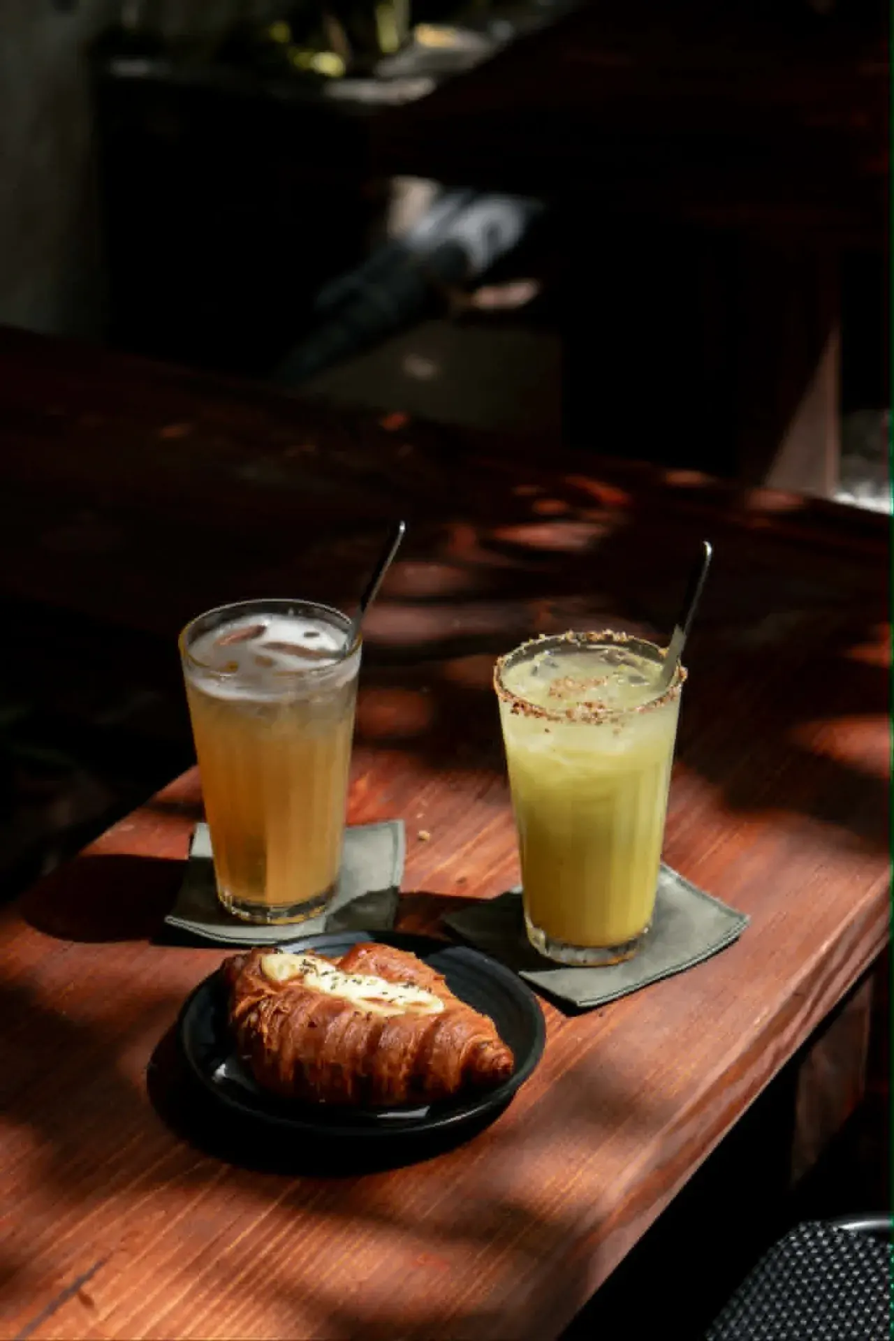 Cold brew và croissant trứng muối / phô mai trên bàn gỗ Cà Viết Hoa