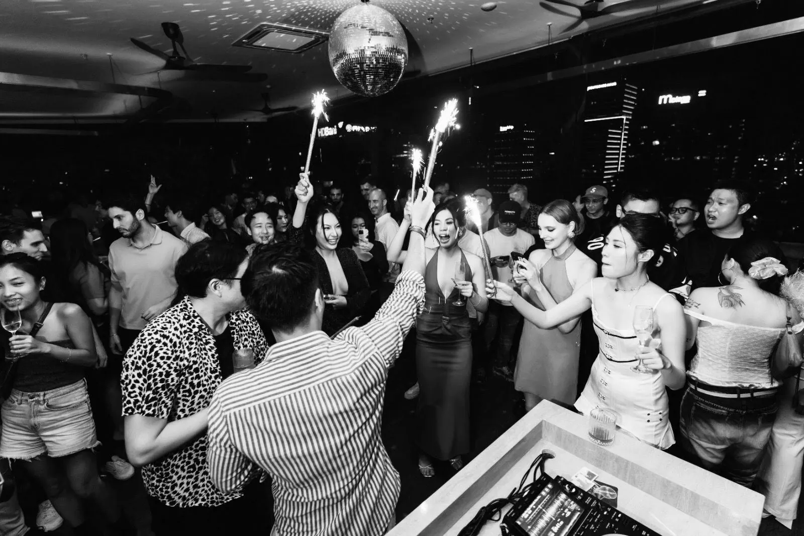 Đám đông sôi động cầm pháo bông trong đêm sự kiện tại Papaya Papa với disco ball và skyline Sài Gòn